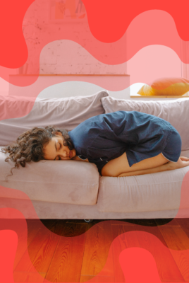 Young woman experiencing period pains curls up living room couch.